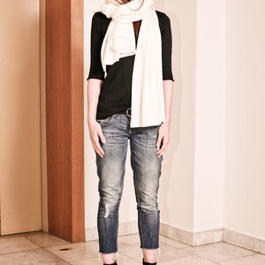 May include: A woman wearing a black long-sleeved shirt, white scarf, blue jeans, and black ankle boots.