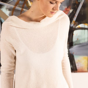 May include: A white off-the-shoulder sweater with long sleeves and a relaxed fit. The sweater is made of a soft, lightweight fabric and has a slightly cropped length.
