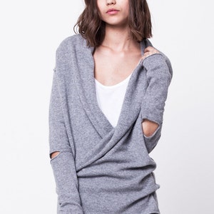 May include: A gray wrap sweater with long sleeves and a V-neck. The sleeves have a distressed look with holes at the elbows.
