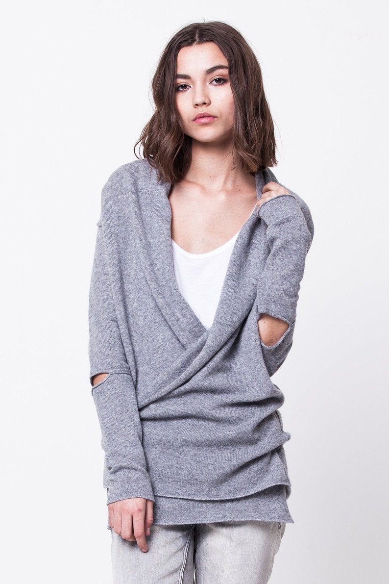 May include: A gray wrap sweater with long sleeves and a V-neck. The sleeves have a distressed look with holes at the elbows.