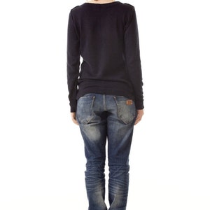 May include: A dark navy blue long-sleeved sweater paired with blue denim jeans featuring a faded wash, back pockets, and a small brown leather patch on the waistband, worn with black ankle boots that have a visible heel and back zipper detail.