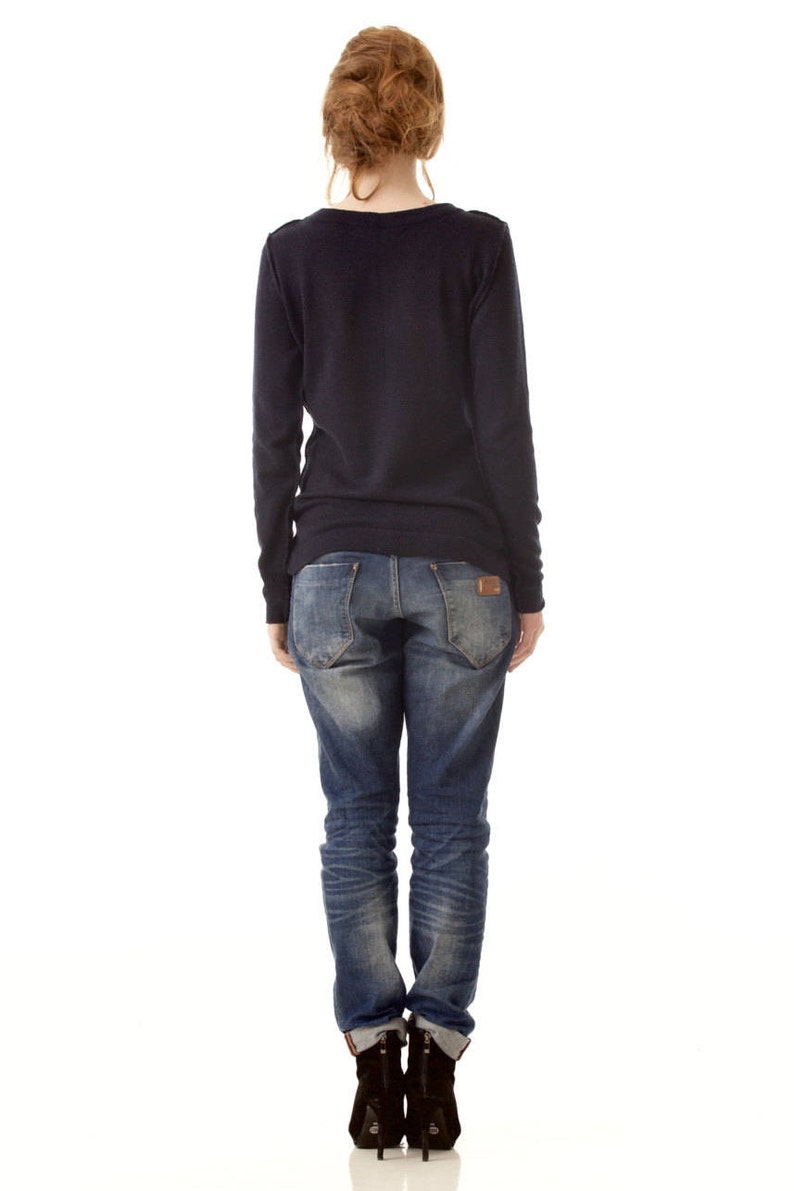 May include: A dark navy blue long-sleeved sweater paired with blue denim jeans featuring a faded wash, back pockets, and a small brown leather patch on the waistband, worn with black ankle boots that have a visible heel and back zipper detail.