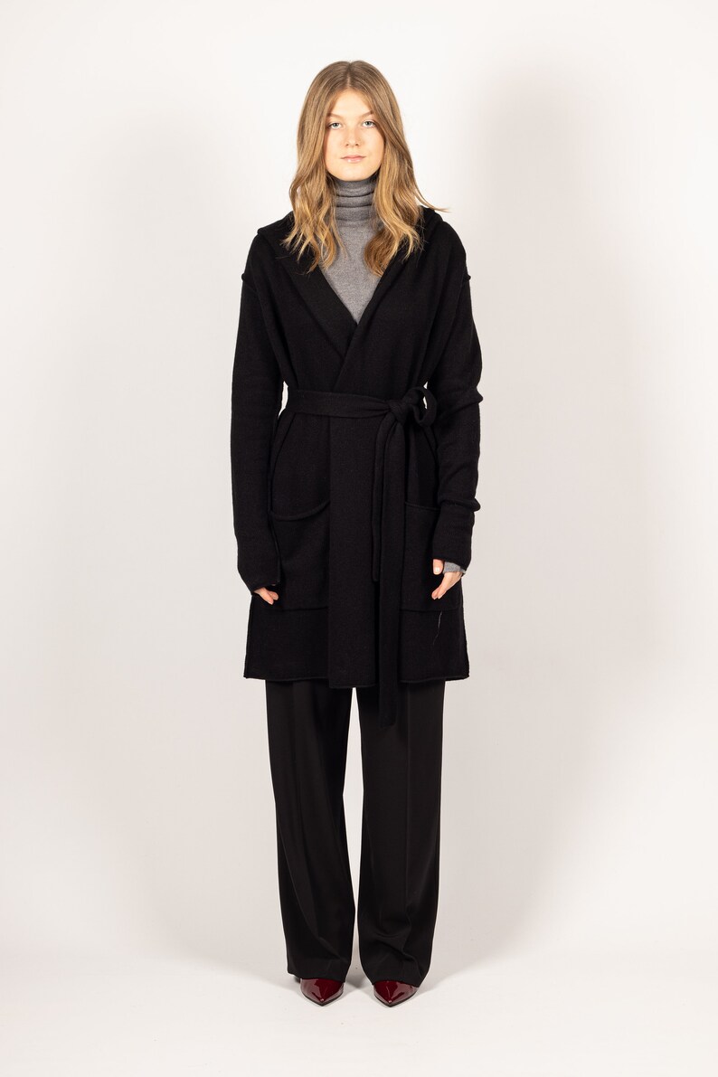 Make a statement in the EDITH black hooded cashmere cardigan or jacket from Krista Elsta, showcasing a stylish and elongated silhouette.