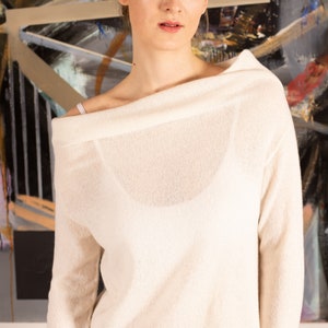 May include: A white off-the-shoulder sweater with long sleeves. The sweater is made of a soft, lightweight fabric and has a relaxed fit.