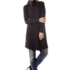 Peut inclure: Un pull tunique bleu marine à manches longues avec un col roulé. Le pull est associé à un jean bleu et des bottines noires à talons hauts. Le modèle est sur fond blanc.