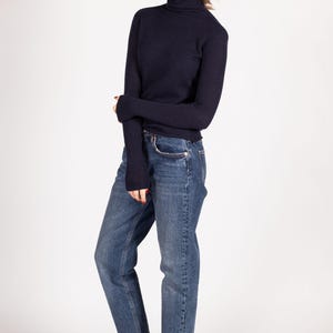 May include: A dark navy blue long-sleeved turtleneck sweater paired with medium-wash blue denim jeans and white sneakers. The sweater features a fitted silhouette with long sleeves, while the jeans have a straight-leg cut and a classic five-pocket design.