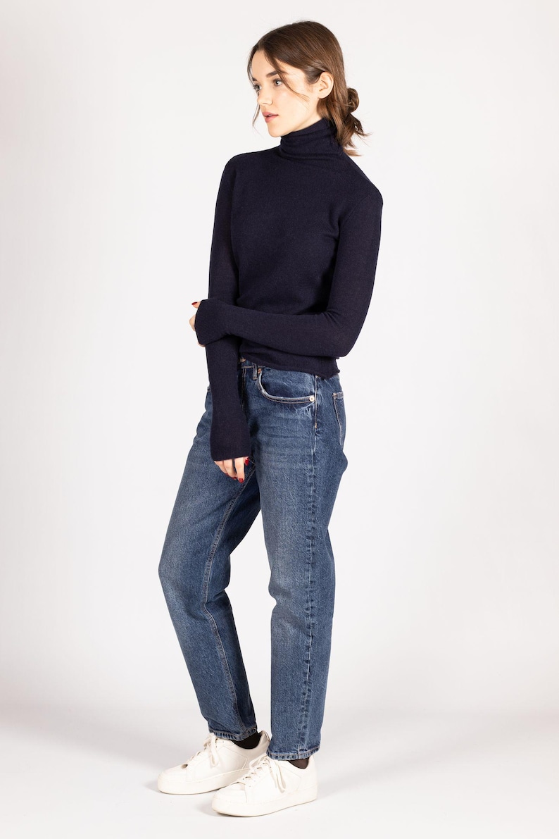 May include: A dark navy blue long-sleeved turtleneck sweater paired with medium-wash blue denim jeans and white sneakers. The sweater features a fitted silhouette with long sleeves, while the jeans have a straight-leg cut and a classic five-pocket design.