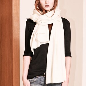 May include: A woman wearing a white scarf over a black long-sleeved shirt and blue jeans.