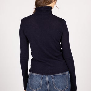 May include: A dark navy blue long-sleeved turtleneck sweater made of a fine-knit fabric. The sweater features a fitted silhouette with a high neck that folds over, long sleeves that extend to the wrists, and a straight hemline at the waist.