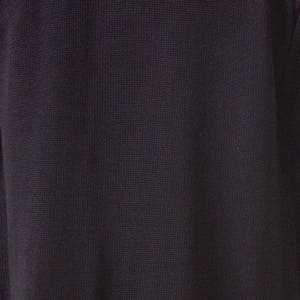 May include: Close-up of a dark navy blue knit fabric. The texture of the material is visible, with a subtle grid-like pattern. The fabric appears to be soft and possibly a sweater or other garment.