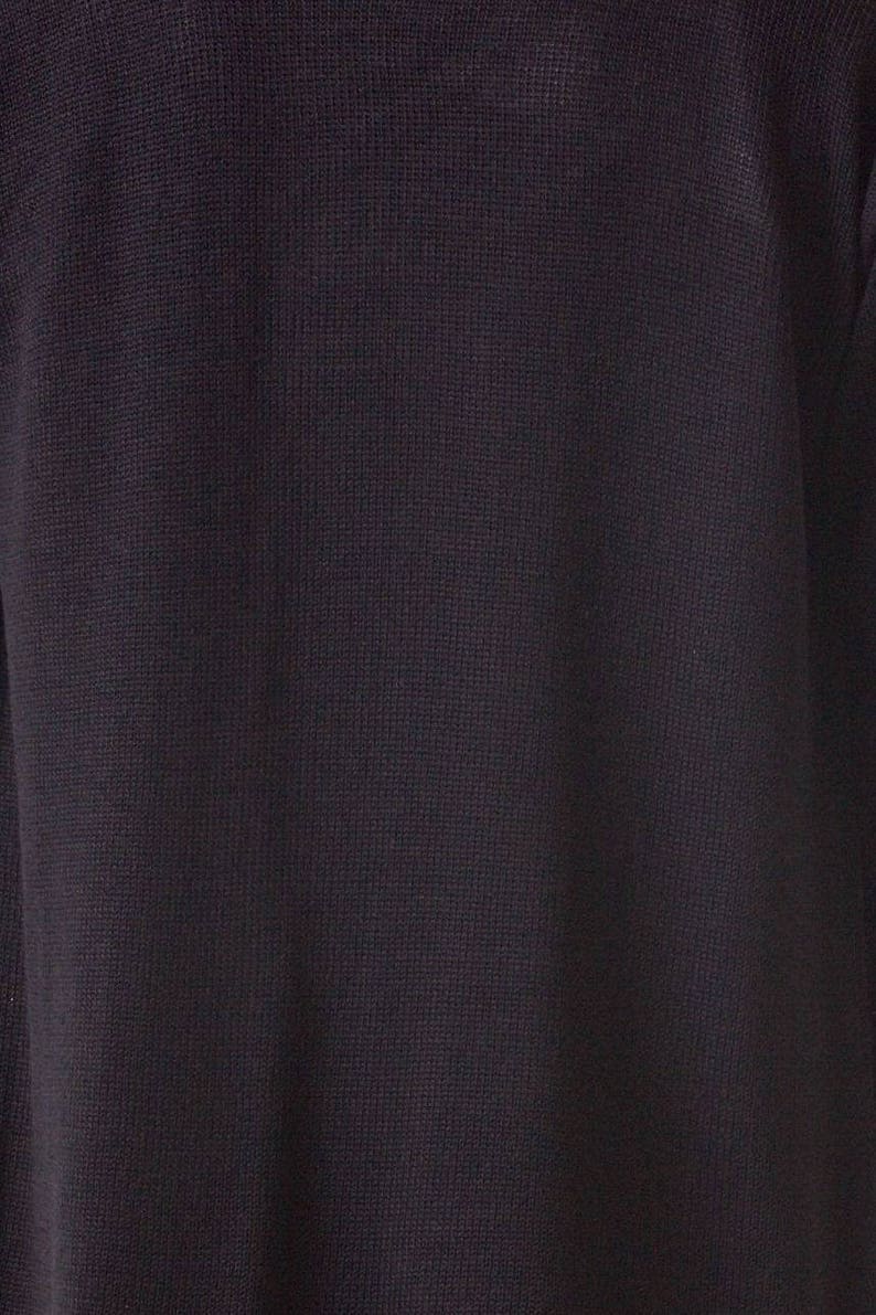 May include: Close-up of a dark navy blue knit fabric. The texture of the material is visible, with a subtle grid-like pattern. The fabric appears to be soft and possibly a sweater or other garment.