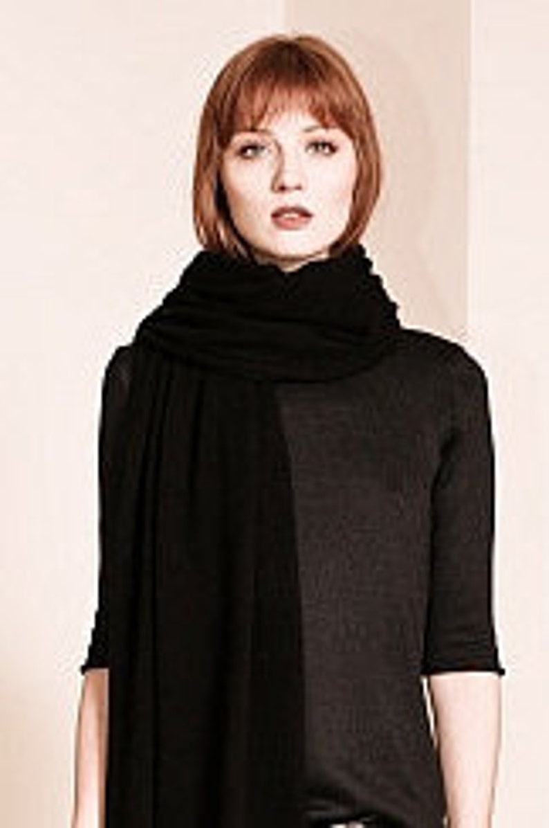 May include: A black cashmere scarf draped around a person's neck. The scarf is soft and luxurious, perfect for adding a touch of warmth and style to any outfit.