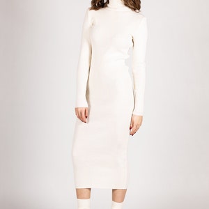 K&ouml;nnte beinhalten: Ein wei&szlig;es, geripptes Rollkragenpulloverkleid mit langen &Auml;rmeln. Das Kleid ist figurbetont und reicht bis zur Mitte der Wade. Das Model tr&auml;gt schwarze Plateauschuhe mit wei&szlig;en Socken.