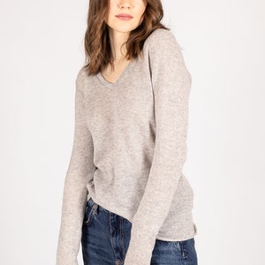 May include: A light gray long-sleeved sweater with a v-neck. The sweater is made of a soft, comfortable material and has a relaxed fit.