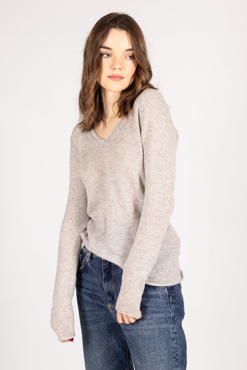 May include: A light gray long-sleeved sweater with a v-neck. The sweater is made of a soft, comfortable material and has a relaxed fit.