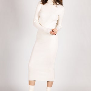 K&ouml;nnte beinhalten: Ein wei&szlig;es Rollkragenpulloverkleid mit gerippter Struktur. Das Kleid ist figurbetont und reicht bis zur Mitte der Wade. Das Model tr&auml;gt schwarze Plateau-Heels mit wei&szlig;en Socken.