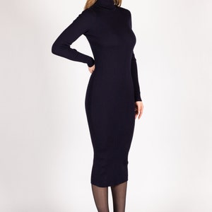 Op de afbeelding: Een marineblauwe geribbelde midi-jurk met een hoge hals en lange mouwen. De jurk is aangesloten en heeft een eenvoudig, elegant ontwerp.