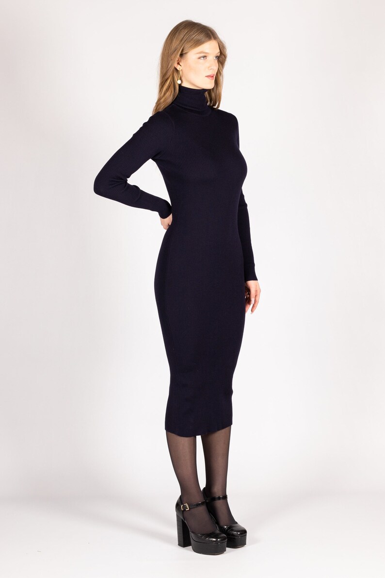 Op de afbeelding: Een marineblauwe geribbelde midi-jurk met een hoge hals en lange mouwen. De jurk is aangesloten en heeft een eenvoudig, elegant ontwerp.