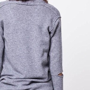 May include: A gray long-sleeved sweater with a distressed detail on the elbow. The sweater is made of a soft, knit fabric.