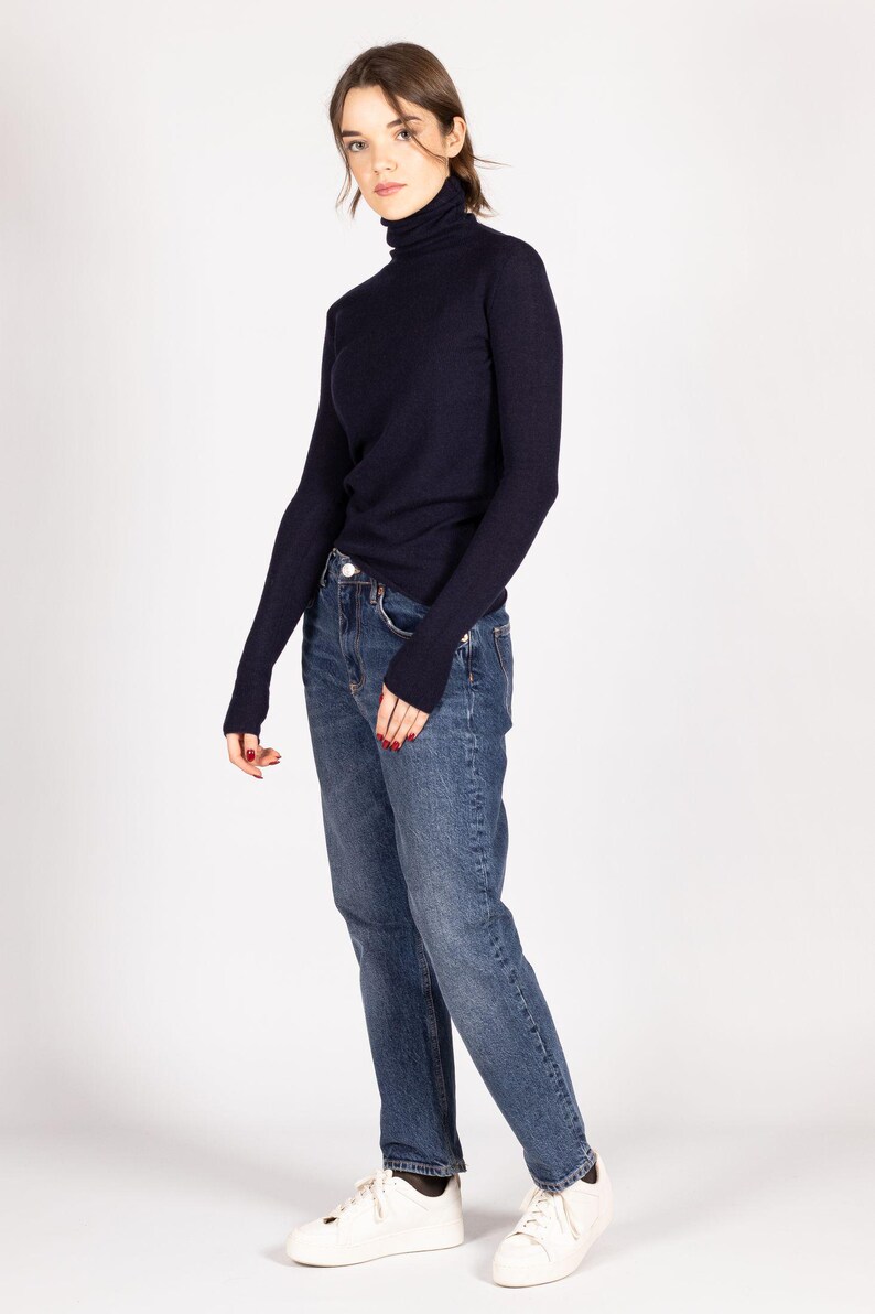 May include: A dark navy blue long-sleeve turtleneck sweater paired with medium-wash blue denim jeans and white sneakers. The sweater features a fitted silhouette with a high neck, while the jeans have a straight-leg cut and a classic button fly.