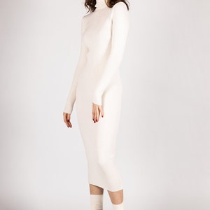 K&ouml;nnte beinhalten: Ein wei&szlig;es, geripptes Rollkragenpulloverkleid mit langen &Auml;rmeln. Das Kleid ist figurbetont und reicht bis zur Mitte der Wade. Das Model tr&auml;gt wei&szlig;e Socken und schwarze Plateauschuhe.