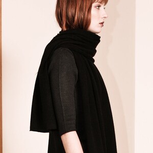 May include: A woman wearing a black long-sleeved shirt and a black scarf. The scarf is folded and draped around her neck.