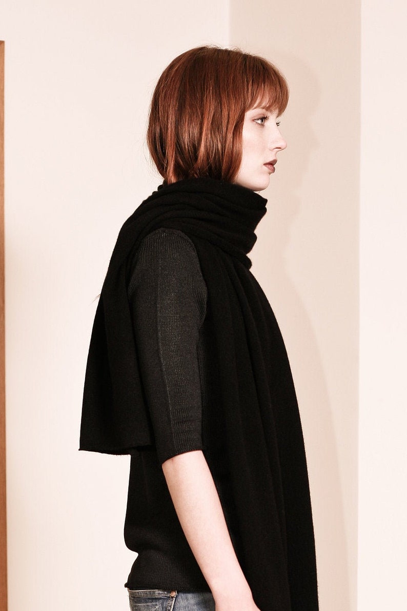 May include: A woman wearing a black long-sleeved shirt and a black scarf. The scarf is folded and draped around her neck.