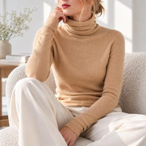 May include: A long-sleeved, tan-colored turtleneck sweater featuring a fitted silhouette and a ribbed collar. The garment is crafted from a soft, fine-knit fabric and is paired with loose-fitting, off-white trousers that have a smooth texture.