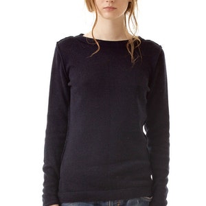 May include: A long-sleeved, dark navy blue knit sweater featuring a wide boat neckline and visible seam detailing along the shoulders and sides. The sweater is paired with blue denim jeans that have a distressed, worn-in texture and a faded wash.
