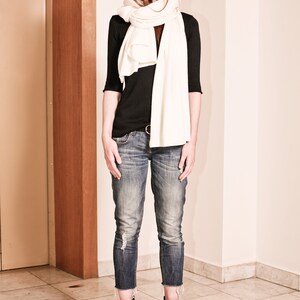 May include: A woman wearing a white scarf, a black long-sleeved shirt, blue jeans, and black ankle boots.