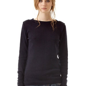 May include: A long-sleeved, dark navy blue knit sweater featuring a simple crew neckline and visible vertical seam detailing down the center front, paired with distressed blue denim jeans that have a small frayed hole on the right thigh area.