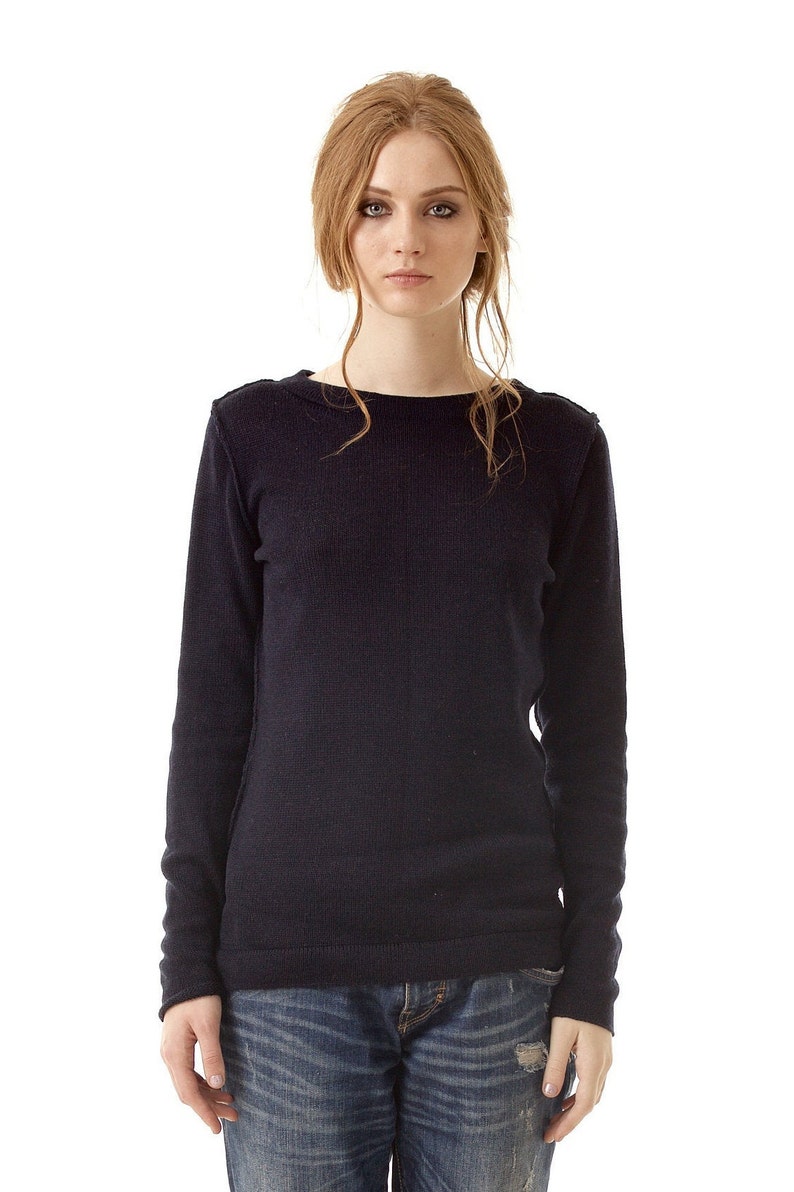 May include: A long-sleeved, dark navy blue knit sweater featuring a simple crew neckline and visible vertical seam detailing down the center front, paired with distressed blue denim jeans that have a small frayed hole on the right thigh area.