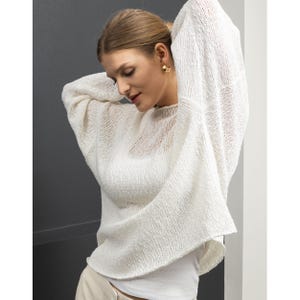 May include: A white, loose-fitting knit sweater with a slightly cropped hem. The sweater is made of a lightweight, open-weave fabric.