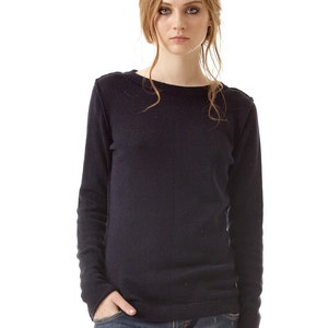 May include: A long-sleeved, dark navy blue knit sweater with a simple crew neckline, paired with blue denim jeans that feature a distressed, worn-in texture and a small rip on the front thigh area, creating a casual and functional everyday outfit.
