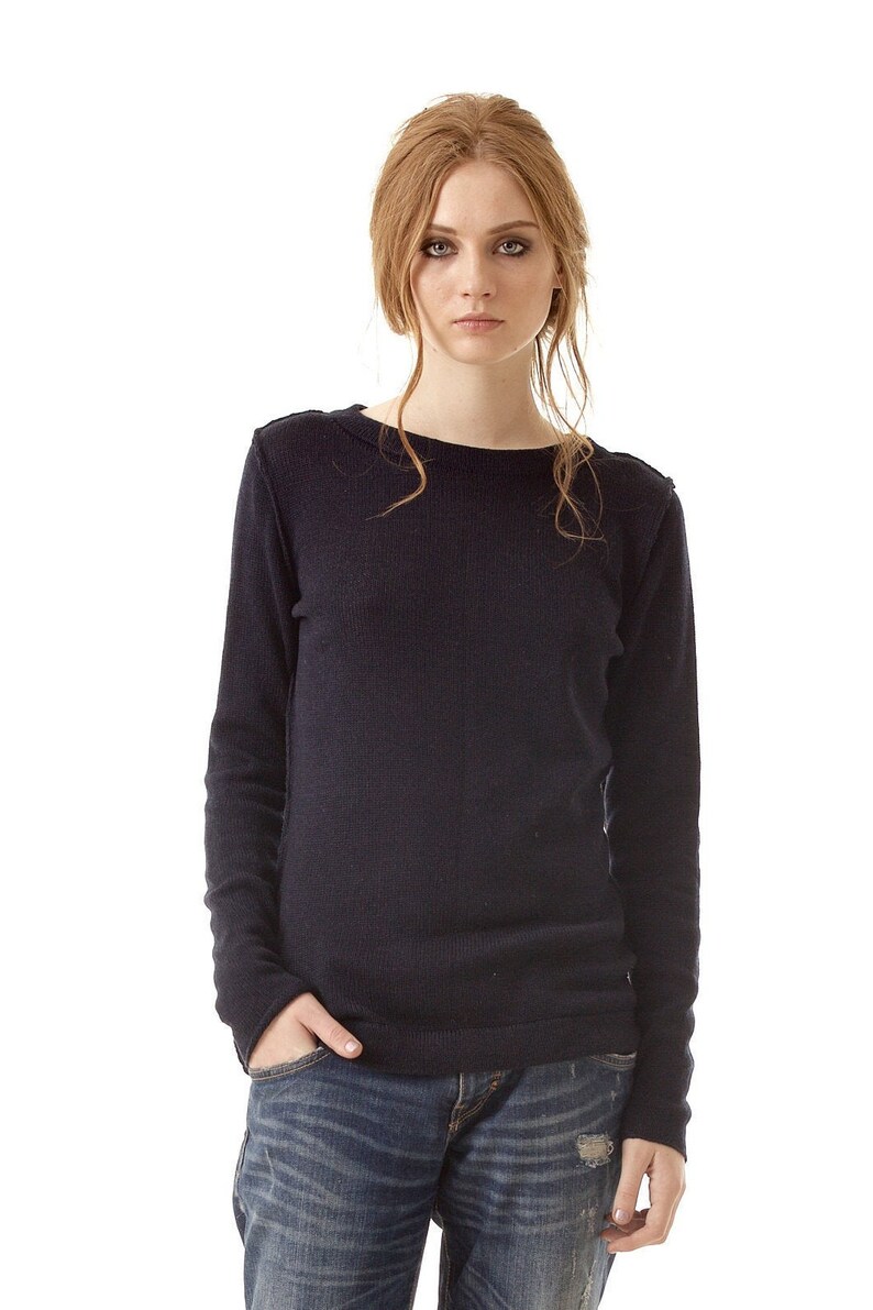 May include: A long-sleeved, dark navy blue knit sweater with a simple crew neckline, paired with blue denim jeans that feature a distressed, worn-in texture and a small rip on the front thigh area, creating a casual and functional everyday outfit.
