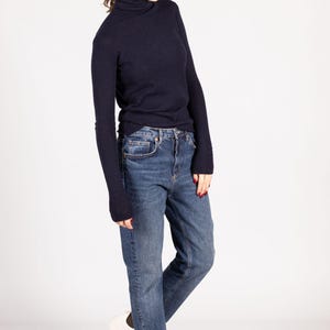 May include: A dark navy blue long-sleeve turtleneck sweater paired with medium-wash blue denim jeans and white sneakers. The sweater features a fitted silhouette with long sleeves, while the jeans have a classic straight-leg cut and a button fly.