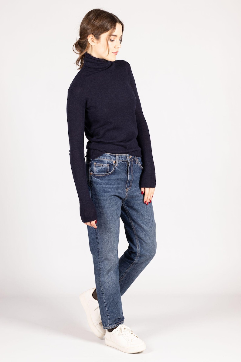 May include: A dark navy blue long-sleeve turtleneck sweater paired with medium-wash blue denim jeans and white sneakers. The sweater features a fitted silhouette with long sleeves, while the jeans have a classic straight-leg cut and a button fly.