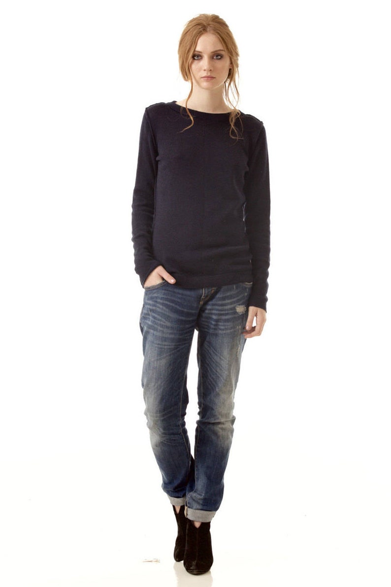 May include: A long-sleeved dark navy blue crew neck sweater paired with blue denim jeans featuring a distressed wash and cuffed hems, complemented by black ankle boots. The ensemble presents a casual look with a solid-colored top.