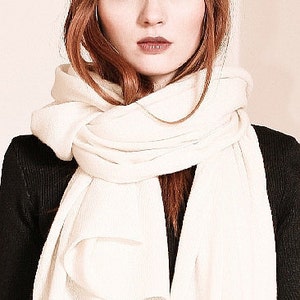 May include: A woman with red hair wearing a white knitted scarf. The scarf is wrapped around her neck and tied in a loose knot.