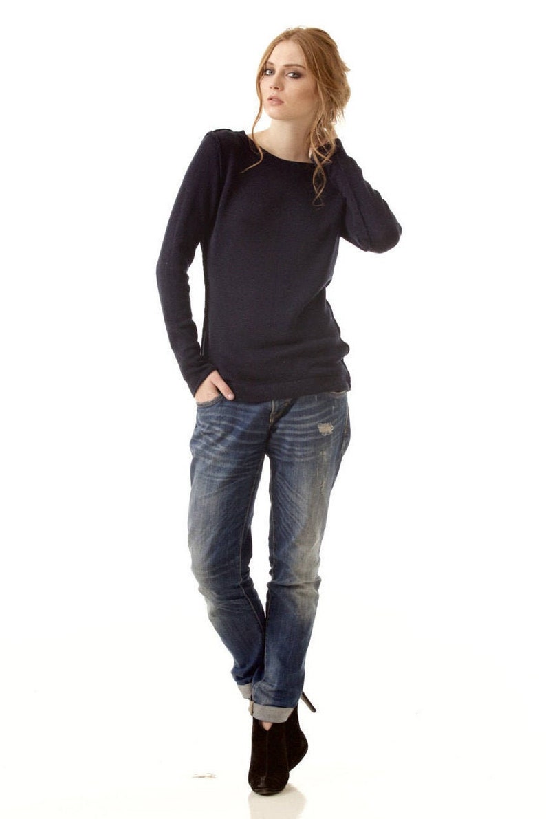 May include: A long-sleeved navy blue sweater with a round neckline paired with blue denim jeans featuring a distressed finish and rolled cuffs, complemented by black ankle boots with a pointed toe and a slim heel.
