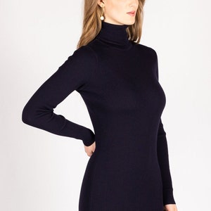 Op de afbeelding: Een lange, donkerblauwe trui met hoge hals van geribbelde brei.