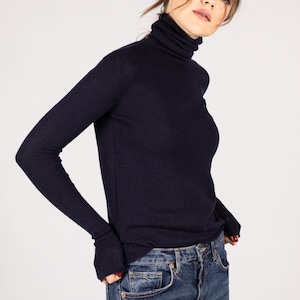 May include: A dark navy blue long-sleeve turtleneck sweater with a fitted silhouette and ribbed texture, paired with classic blue denim jeans featuring a button fly and traditional five-pocket construction with copper-colored metal rivets.