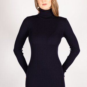 Op de afbeelding: Een donkerblauwe trui-jurk met een hoge hals, lange mouwen en een aansluitende pasvorm.