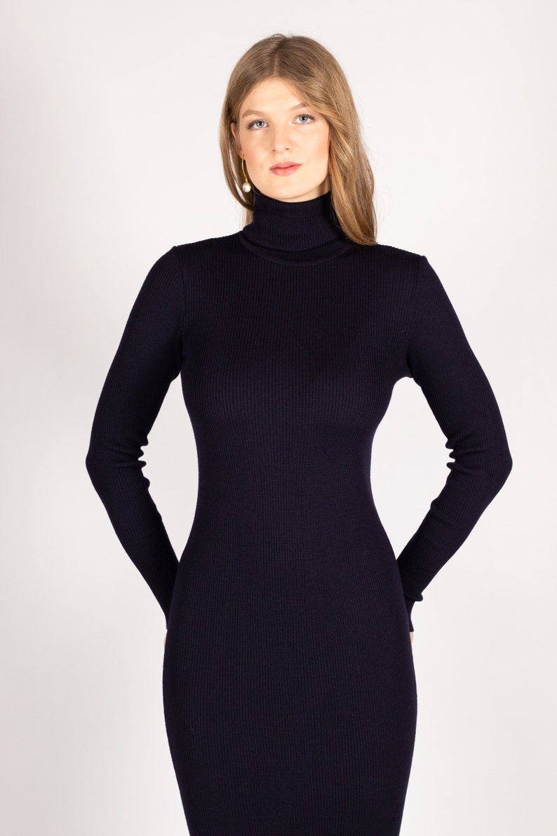Op de afbeelding: Een donkerblauwe trui-jurk met een hoge hals, lange mouwen en een aansluitende pasvorm.