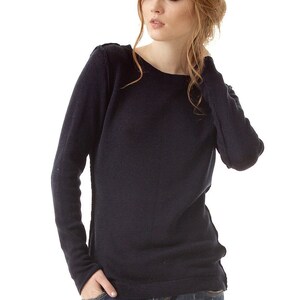 May include: A long-sleeved navy blue knit sweater featuring a wide boat neckline and visible seam detailing along the shoulders and sides, paired with distressed blue denim jeans that have a worn-in texture and a small rip on the front thigh area.
