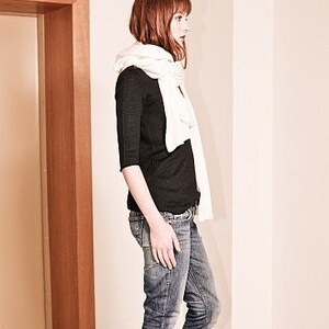 May include: A woman wearing a black long-sleeved shirt, blue jeans, and a white scarf.