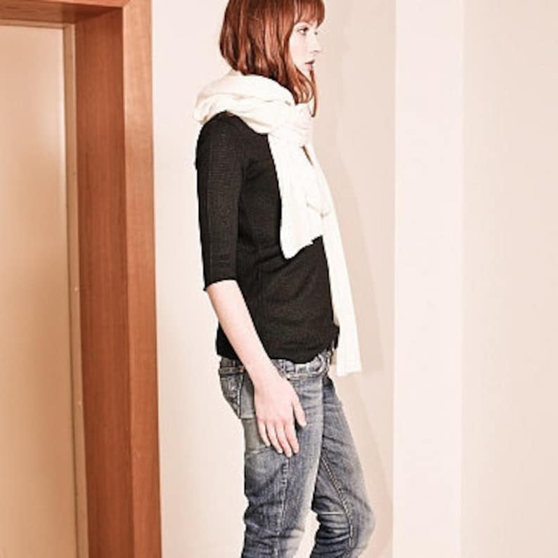 May include: A woman wearing a black long-sleeved shirt, blue jeans, and a white scarf.