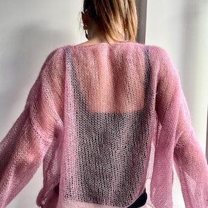 Puede incluir: Un su&eacute;ter rosa claro y transparente con mangas largas. El su&eacute;ter tiene un dise&ntilde;o de punto suelto y abierto, que revela la ropa de abajo. La prenda es ligera y parece estar hecha de un material suave y delicado.