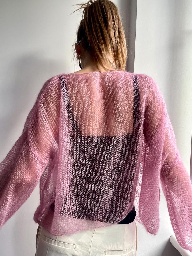 Puede incluir: Un su&eacute;ter rosa claro y transparente con mangas largas. El su&eacute;ter tiene un dise&ntilde;o de punto suelto y abierto, que revela la ropa de abajo. La prenda es ligera y parece estar hecha de un material suave y delicado.