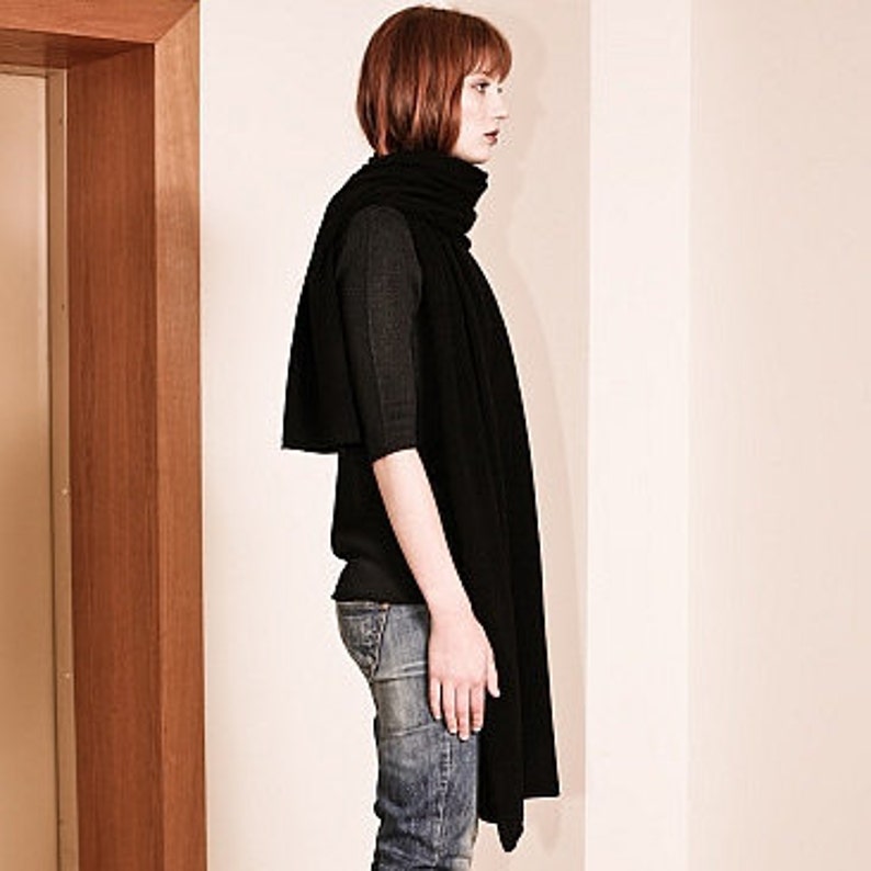 May include: A black knit scarf draped around a person's neck. The scarf is long and wide, and it is made of a soft, textured fabric.